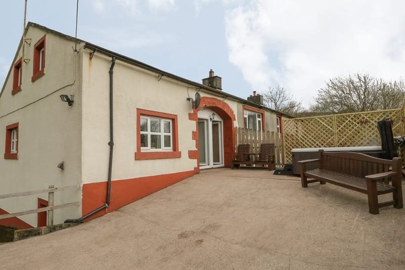 Cream house with red trim and arched doorway; outdoor seating on a paved patio with wooden benches.