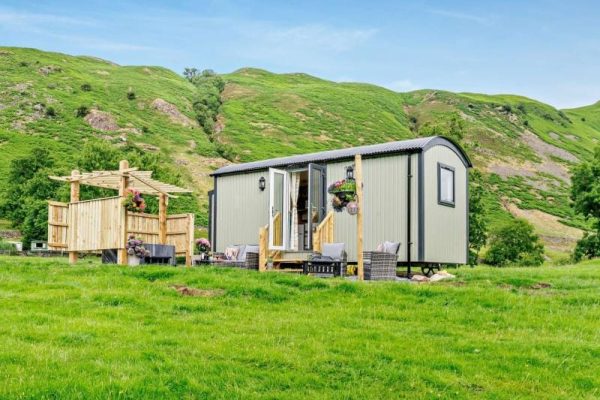 A small, modern mobile home with a wooden deck and outdoor seating in a lush green valley.
