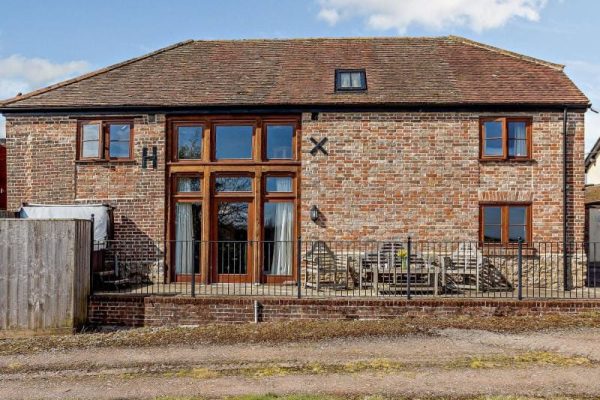 Brick house with a central glass entry, brick facade, and a fenced patio with outdoor furniture on a sunny day.