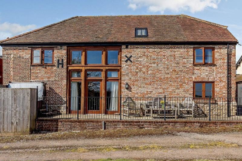 Brick house with a central glass entry, brick facade, and a fenced patio with outdoor furniture on a sunny day.