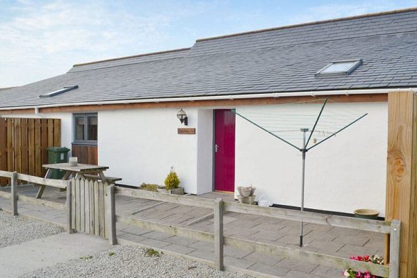 White single-story house with a bright pink door, an outdoor rotary clothesline, and a wooden fence courtyard.
