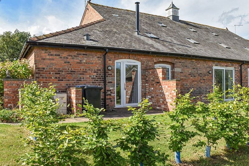 Brick one-story house with a tiled sloped roof, glass door, and garden in front; green shrubs line the lawn.