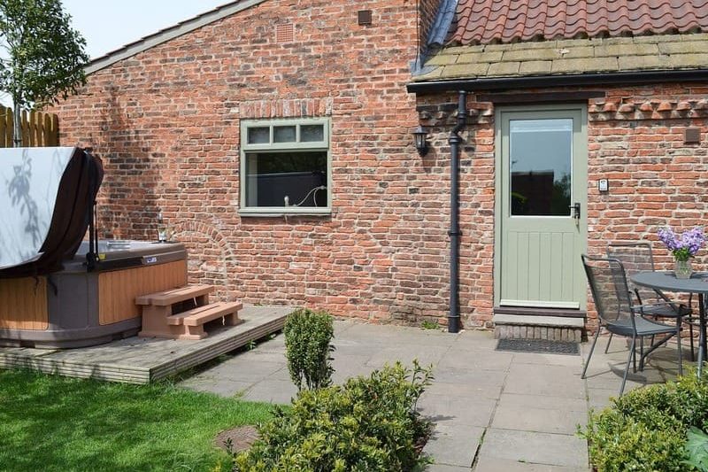 Brick backyard with a hot tub on a wooden deck, steps leading up, and a pale green door beside a window.