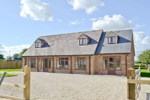 Brick house with slate roof and dormer windows, gravel driveway, and wooden gate in a rural setting