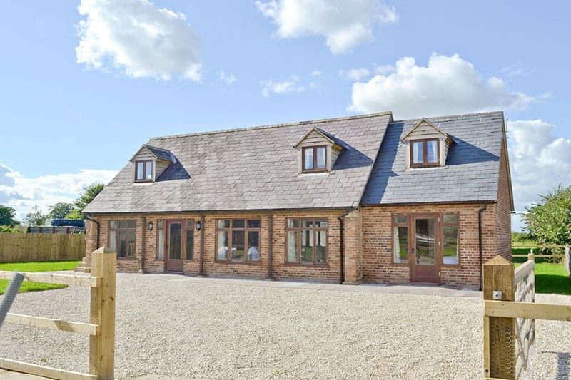 Brick house with slate roof and dormer windows, gravel driveway, and wooden gate in a rural setting